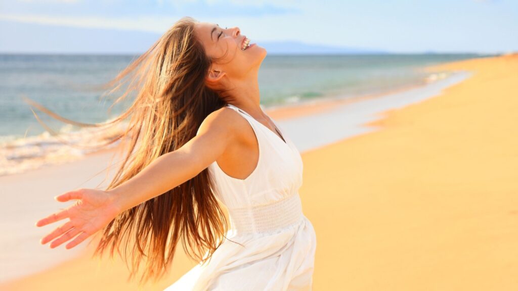 a stress free woman on the beach with her arms open wide