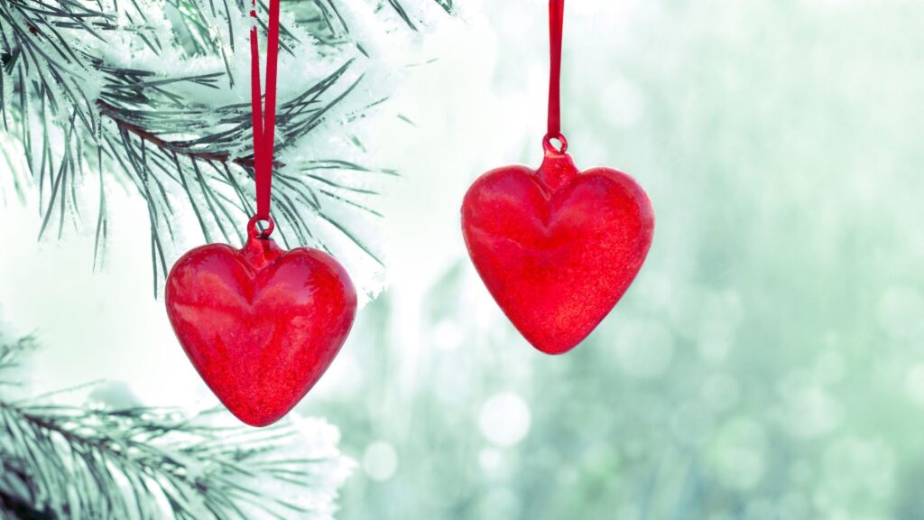 two red heart ornaments hanging from a christmas tree branch