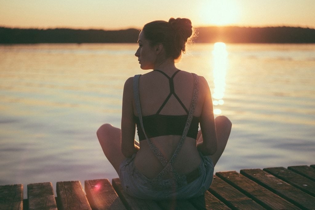 woman sitting on a dock overlooking the lake at sunset