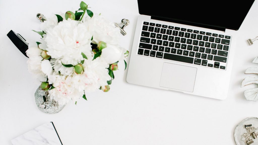 white flowers next to a silver laptop on a white desk