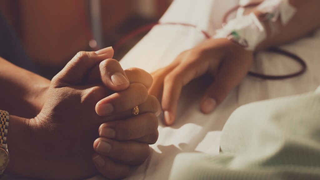 hands folded in prayer laying on the hospital bed of a sick person