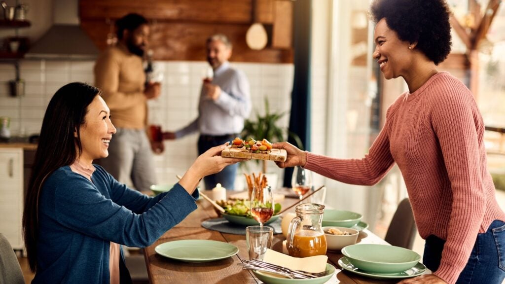 african american woman showing biblical hospitality while serving a meal to friends in her home