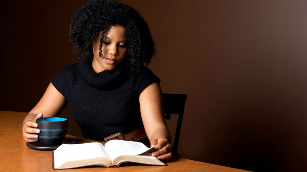 woman sitting at a table reading her Bible and drinking coffee