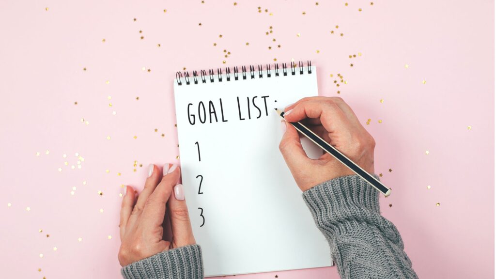 woman's hands writing goals on a notepad