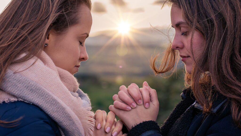 two women praying together outside at sunrise