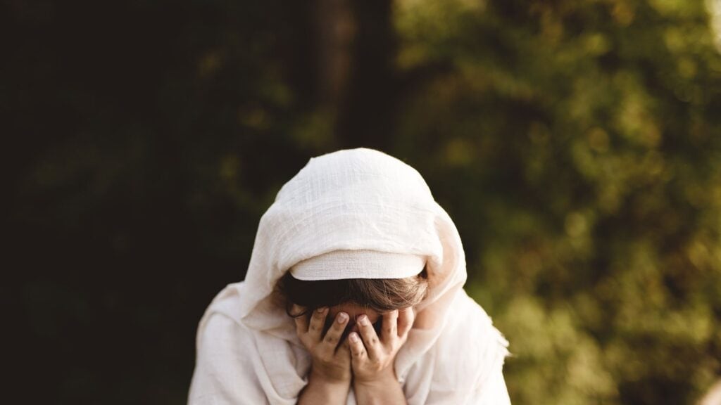 biblical woman in a robe with her hands over her face like she is crying