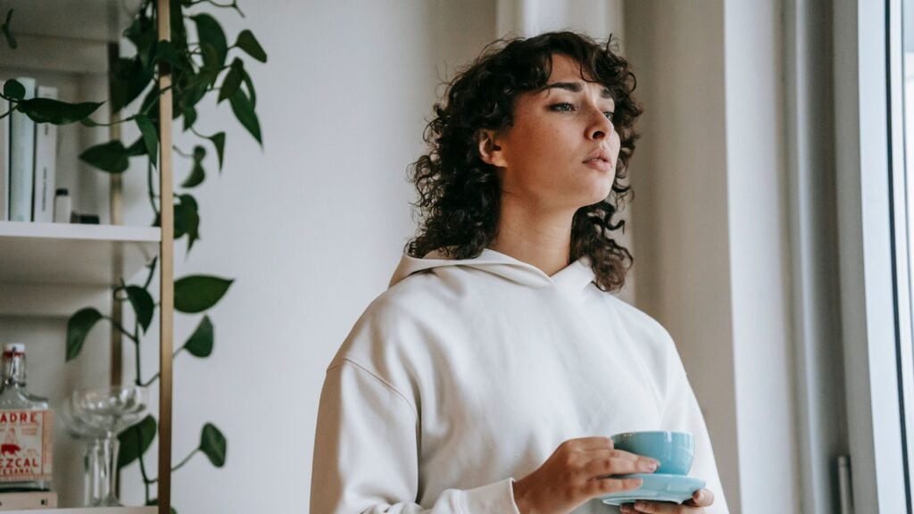 worried woman holding a cup of coffee and staring out the window