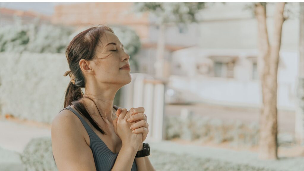 woman standing outside with hands clasped together in prayer