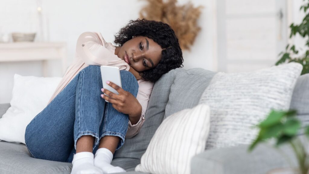woman sitting on her couch looking at her phone